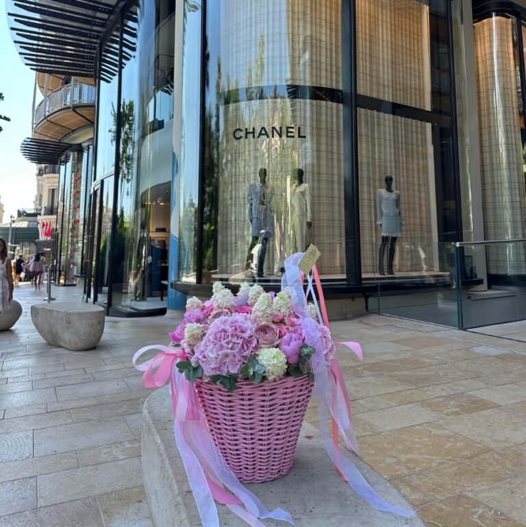 Petite Петит корзина с нежными цветами перед бутиком Chanel на солнечной набережной.