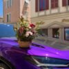 Фиолетовый автомобиль украшен букетом цветов на капоте под ярким солнцем.