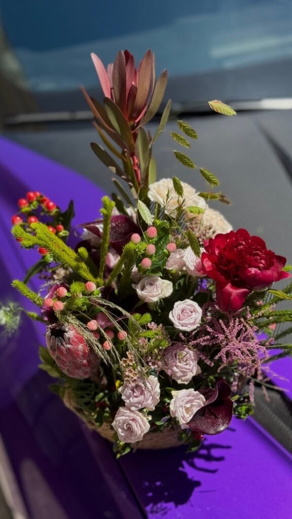 Яркий букет с разнообразными цветами и зеленью на фиолетовом фоне.